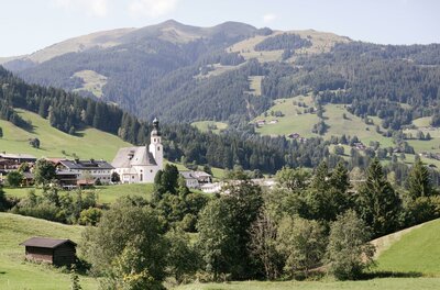 Blick auf das Dorf Jochberg mit seiner Kirche vor bewaldeten Berghängen.