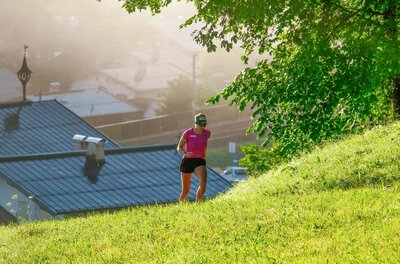 Lisa Hauser beim Lauftraining Eine Läuferin in pinkem Shirt und schwarzer Hose läuft einen grünen Grashang hinauf.
