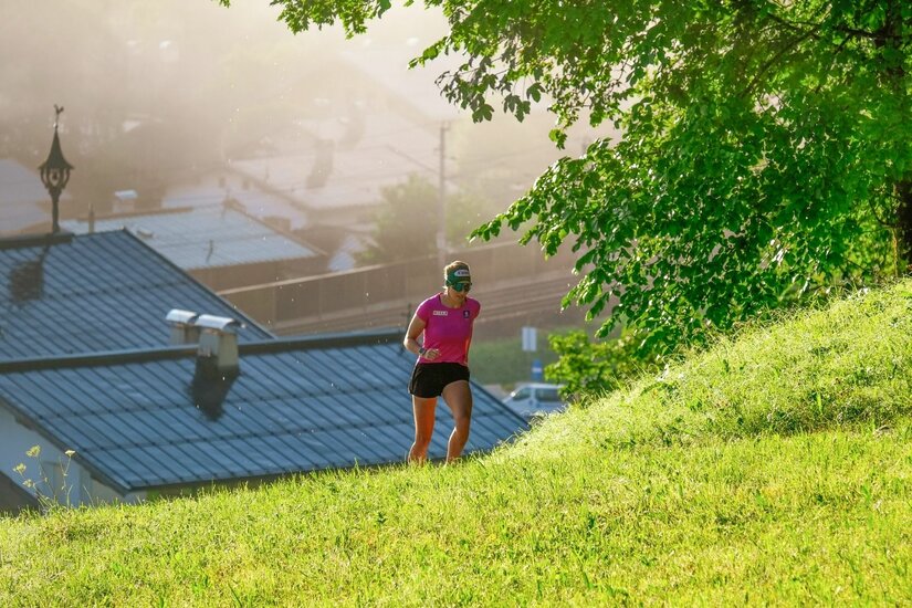 Lisa Hauser beim Lauftraining Eine Läuferin in pinkem Shirt und schwarzer Hose läuft einen grünen Grashang hinauf.