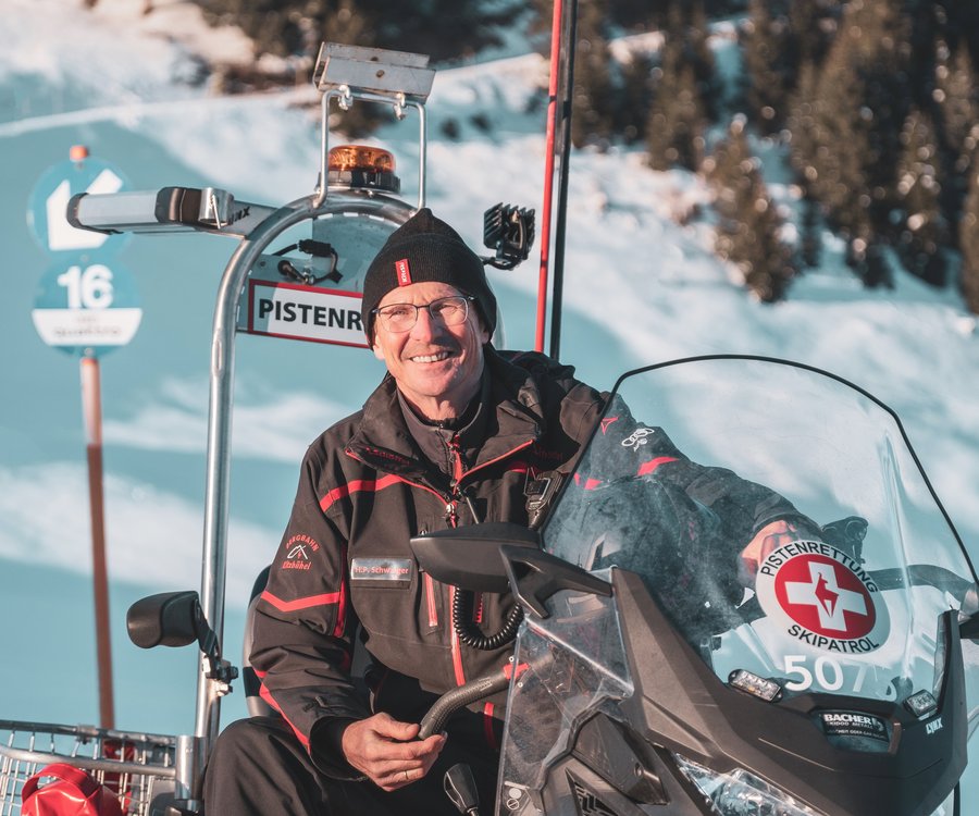 Ein Herr mit Brille sitzt im Schneemobil und lächelt