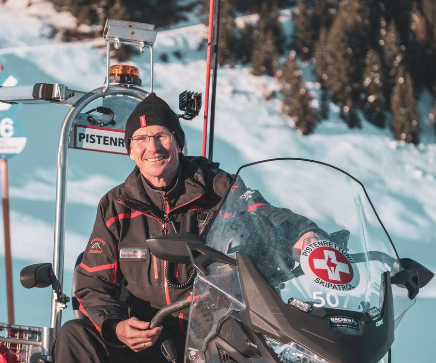 Ein Herr mit Brille sitzt im Schneemobil und lächelt