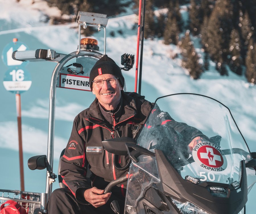 A gentleman with glasses sits in a snowmobile and smiles