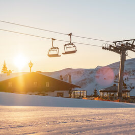 Die untergehende Sonne beleuchtet die verschneite Landschaft, während Sessellifte über die Piste schweben.