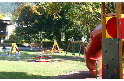 Spielplatz Jochberg Kinderspielplatz mit roter Röhrenrutsche, Karussell und Schaukeln auf einer Rasenfläche.