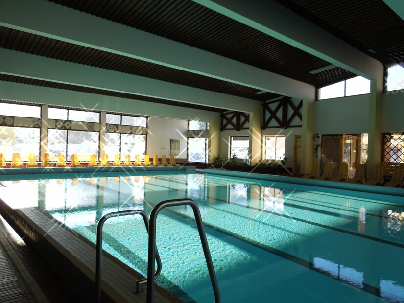 Aubad Fieberbrunn Ein Schwimmbad mit klarem Wasser und einem modernen, hellen Innenraum. Große Fenster sorgen für viel Tageslicht und eine einladende Atmosphäre.