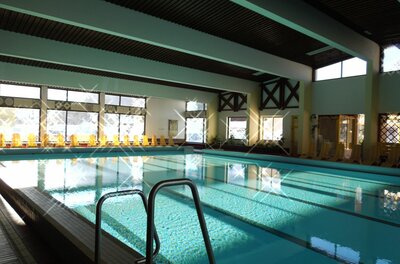 Ein Schwimmbad mit klarem Wasser und einem modernen, hellen Innenraum. Große Fenster sorgen für viel Tageslicht und eine einladende Atmosphäre.