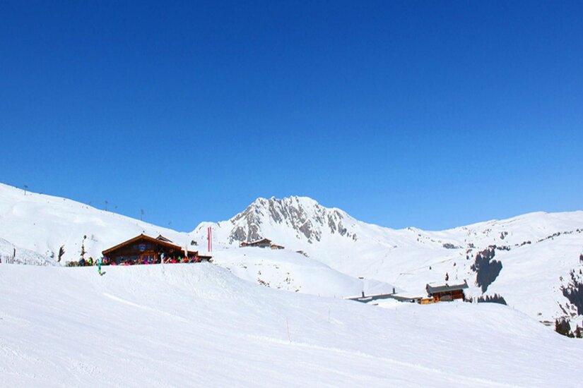 Berghütte Hanglalm im Winter Verschneite Berghütte Hanglalm vor einem felsigen Berggipfel unter blauem Himmel.