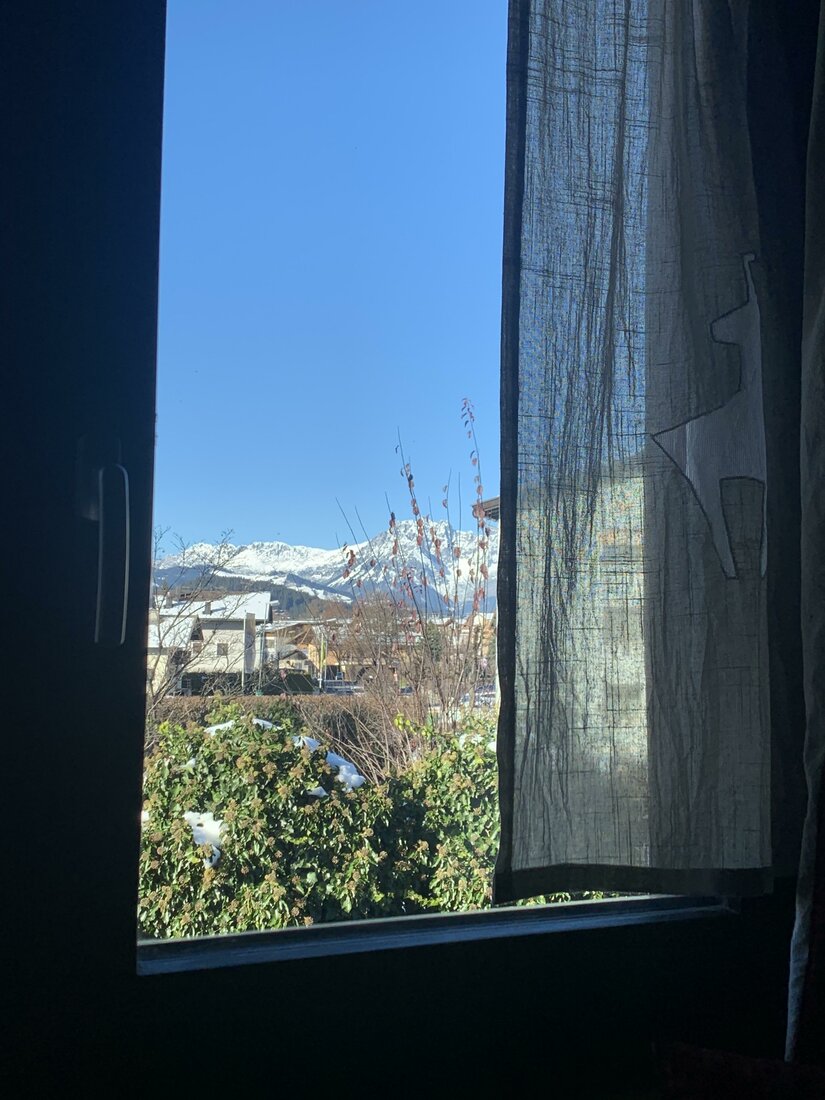 Blick aus einem Fenster auf schneebedeckte Berggipfel unter blauem Himmel.