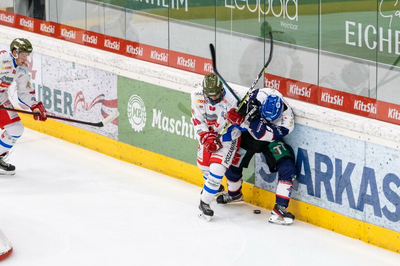 Die Adler Ein spannendes Eishockeyspiel, in dem zwei Spieler um den Puck kämpfen. Einer der Spieler wird an die Bande gedrängt.