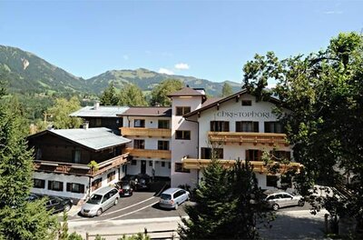 Haus Sommer Christophorus Mehrstöckiges Hotelgebäude mit Holzbalkonen und Parkplatz vor bewaldeter Bergkulisse.