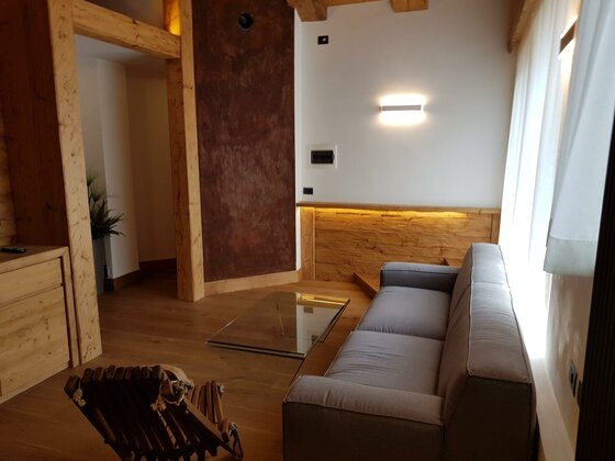 Wohnbereich Apartment Südberge Moderner Wohnbereich mit grauem Sofa, Glastisch und Holzelementen.