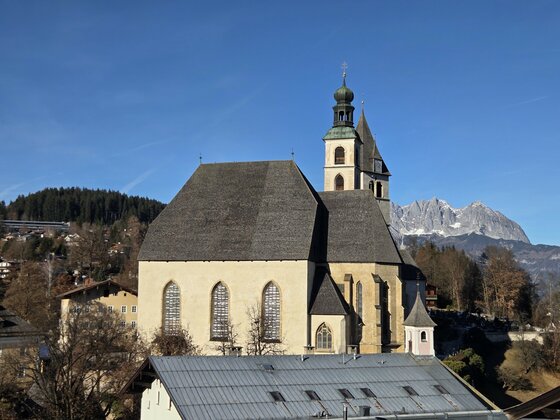 Eine beeindruckende Kirche mit einem markanten Turm in einer malerischen Landschaft. Im Hintergrund sind Berge und ein klarer Himmel zu sehen.