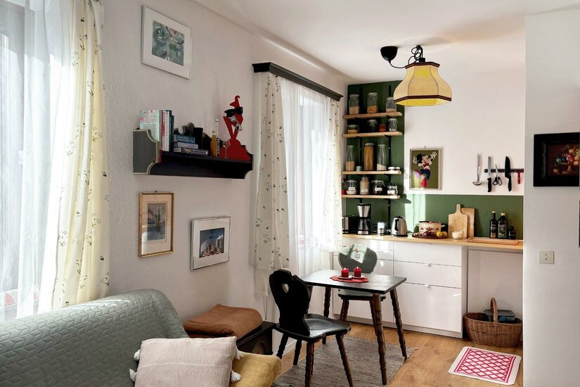 Apartment Alberg und Kathi Ein gemütliches Wohnzimmer mit einer kleinen Essecke und einer Küche im Hintergrund. Helle Farben und eine einladende Atmosphäre prägen den Raum.