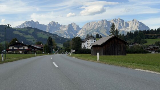 Asphaltierte Landstraße führt auf ein Bergmassiv mit schroffen Felsgipfeln zu.