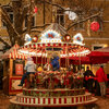 Ein festlich beleuchtetes Karussell mit Kindern, die fröhlich auf den Pferden sitzen, beim Kitzbüheler Adventmarkt in winterlicher Atmosphäre.