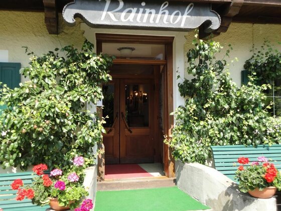 Eingang Pension Rainhof Hölzerner Eingangsbereich der Pension Rainhof mit Blumenkästen und grünen Bänken.