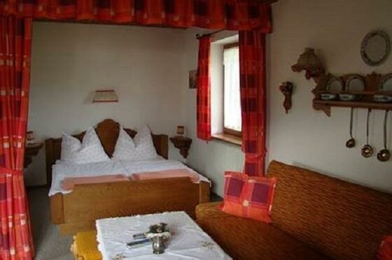 Schlafzimmer App. Hölzl Rustikales Schlafzimmer mit Doppelbett aus Holz, roten Vorhängen und einem Sofa im Vordergrund.