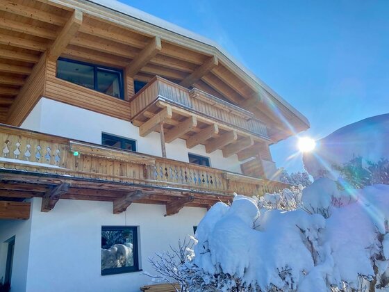 Das Landhaus Barbara im Winter mit schneebedecktem Balkon. Die Sonne scheint hell über dem Gebäude.