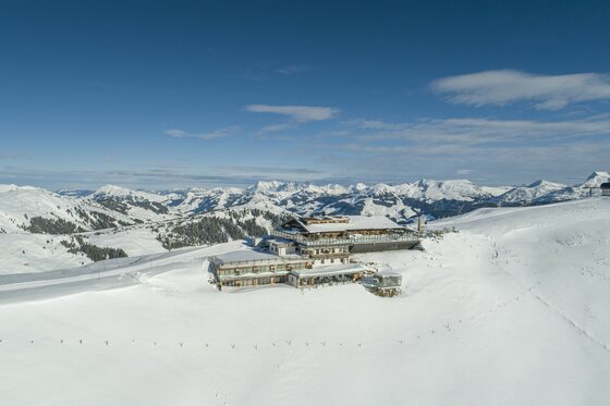 Berghütte in verschneiter Gebirgslandschaft unter blauem Himmel.