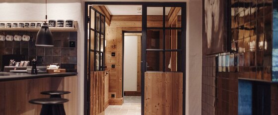 Moderner Innenraum mit Holzwänden, einer Glastür mit schwarzem Rahmen und einer Bar mit Hockern.