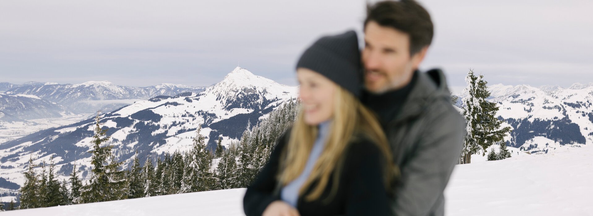 Ein Paar umarmt sich vor der Kulisse der beschneiten Kitzbüheler Alpen