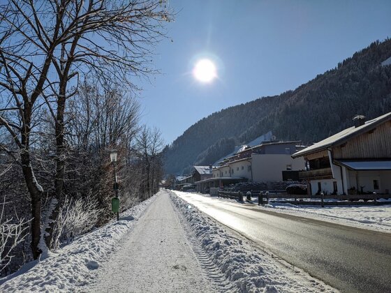 Verschneiter Gehweg neben einer Straße in Malerndörfl bei Sonnenschein.