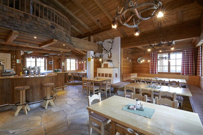 Gaststube Reither Streif Rustikaler Gastraum mit Holztischen, Bar, Kachelofen und Geweih-Lampen.