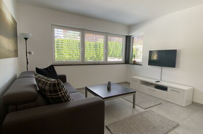 Modernes Wohnzimmer mit dunklem Sofa, Couchtisch, TV an der Wand und hellem Fliesenboden.