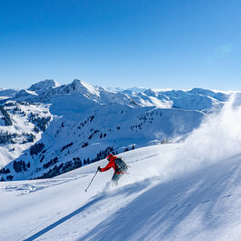In the Kitzbühel ski resort, a skier wearing red is gliding through fresh powder snow in the mountains.