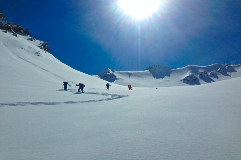 Skiguides Kitzbühel Jochberg Vier Skitourengeher steigen bei Sonnenschein einen verschneiten Hang hinauf.