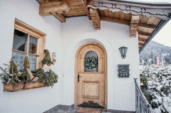 Eingangsbereich eines alpinen Hauses mit Holztür, Fensterkasten und winterlicher Dekoration.