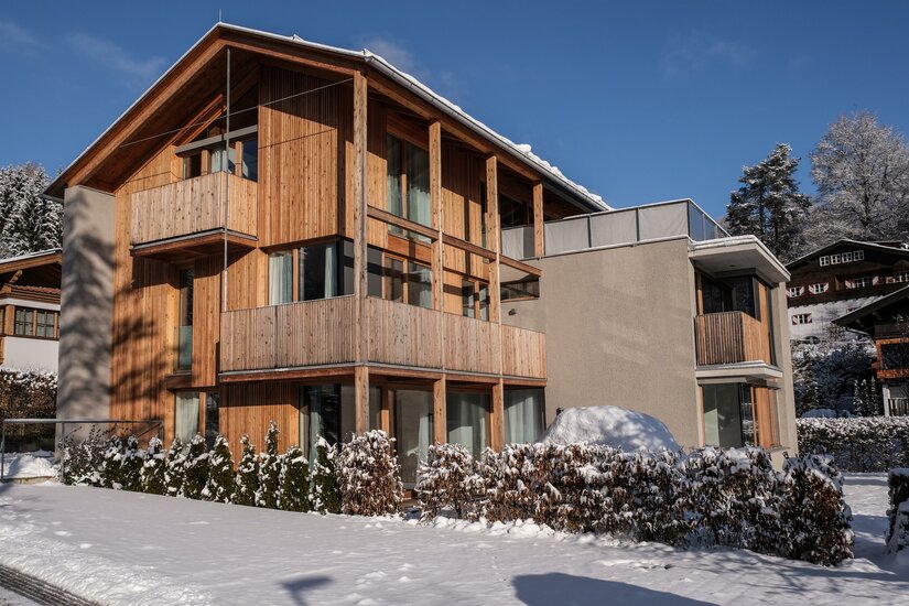 Modernes mehrstöckiges Holzgebäude mit Balkonen im Schnee unter blauem Himmel.