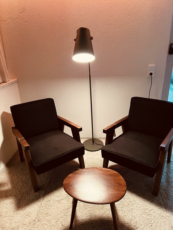 Sitzecke im Pool House Zwei dunkle Sessel mit Holzgestell, ein runder Beistelltisch und eine Stehlampe auf hellem Teppichboden.