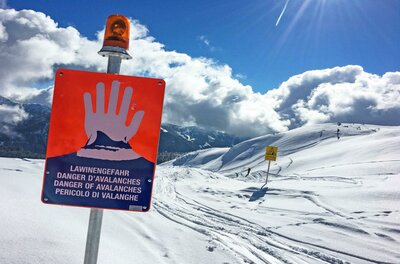 Lawineninformation Ein Warnschild vor Lawinengefahr in einem verschneiten Berggebiet. Die Landschaft ist von Schnee und hohen Bergen umgeben, mit einem klaren Himmel im Hintergrund.