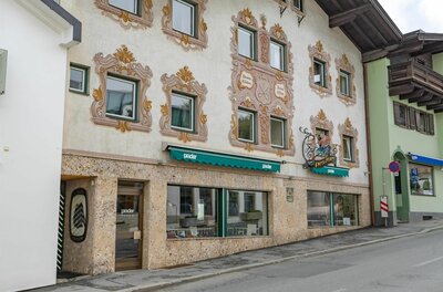 Modehaus Prader Fassade eines Gebäudes mit Wandmalereien um die Fenster und einem Ladengeschäft im Erdgeschoss.