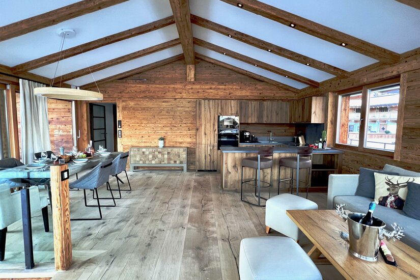 Moderner Wohn- und Essbereich in einem Holzchalet mit offener Küche und Sichtbalken am Dach.