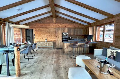 Innenansicht Hideaway Design Chalet Moderner Wohn- und Essbereich in einem Holzchalet mit offener Küche und Sichtbalken am Dach.