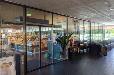 Eingangsbereich einer Baguette Bistro Bäckerei mit Glasschiebetüren und Einkaufswagen.