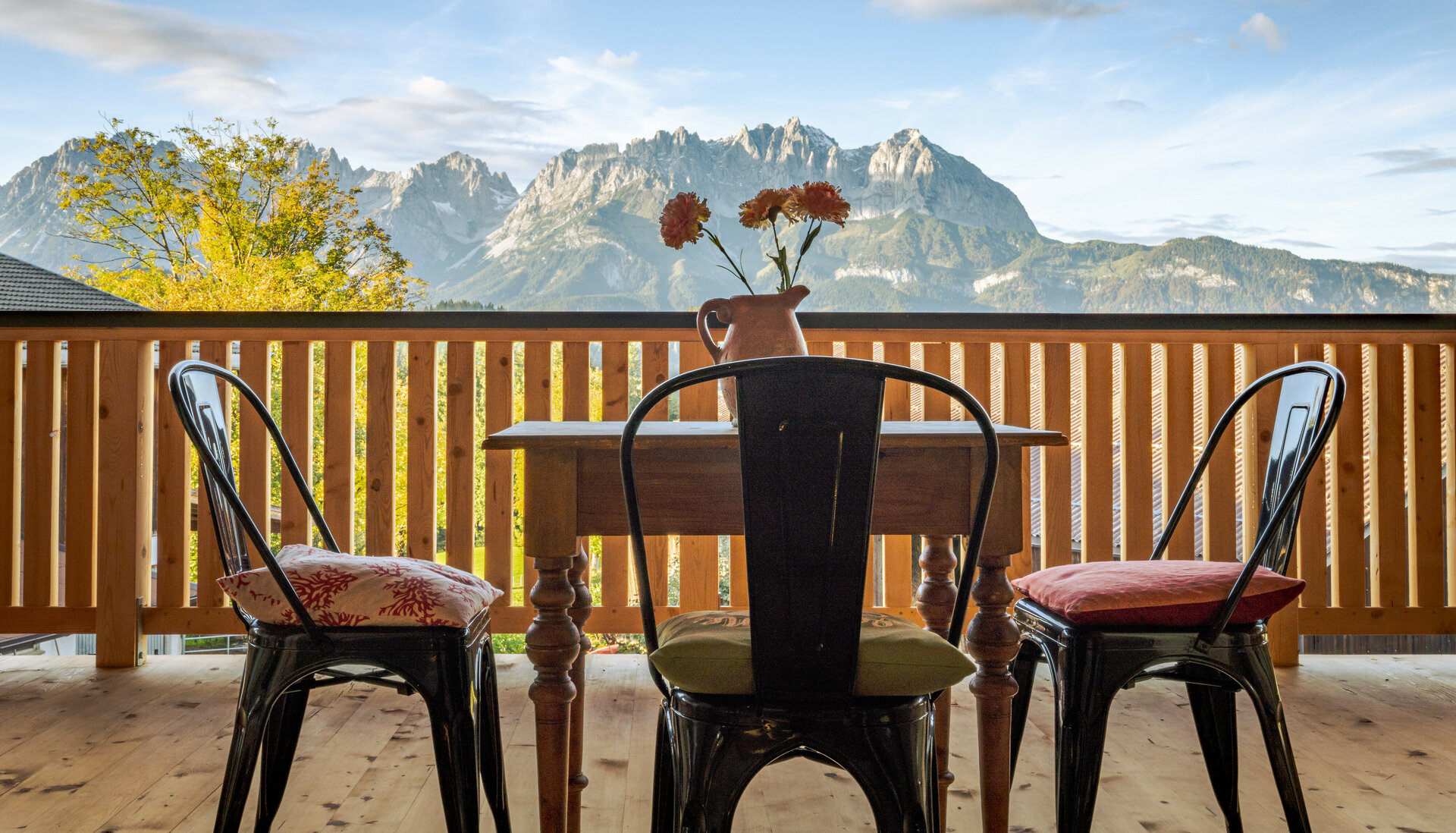 Der Blick von einem Holz-Balkon in Kitzbühel auf das Bergmassiv des Wilden Kaisers, mit einem Tisch und Stühlen, die zum Entspannen einladen.