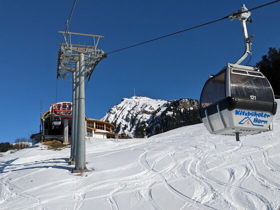Gondel der Kitzbüheler Hornbahn über einer verschneiten Skipiste vor blauem Himmel.