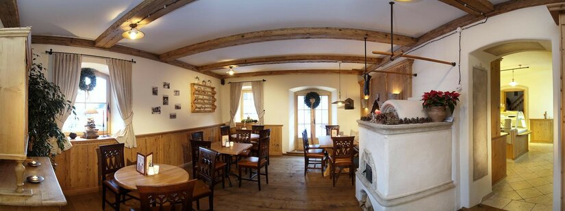 Gastraum Krumma Café Innenansicht eines Cafés mit Holztischen, dunklen Stühlen, einem Kachelofen und Deckenbalken aus Holz.