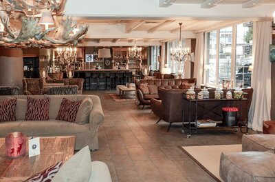Lounge-Bereich mit Ledersofas, Kronleuchtern aus Geweih und einer Bar im Hintergrund.