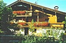 Mehrstöckiges Holzhaus mit Balkonen und Blumenschmuck unter blauem Himmel.