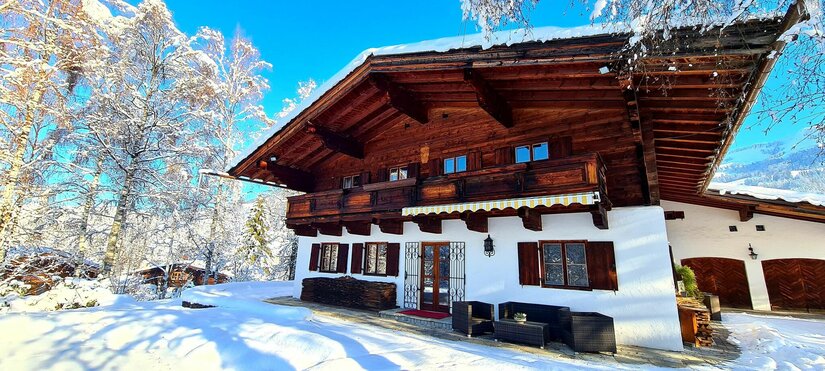 Villa Alpenblick im Winter Alpines Holzhaus mit weißer Fassade in einer verschneiten Winterlandschaft unter blauem Himmel.