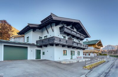 Außenansicht NA-Home Kitzbühel Modernes alpines Wohnhaus mit weißer Fassade, dunklen Holzbalkonen und einer Garage an einer asphaltierten Straße.