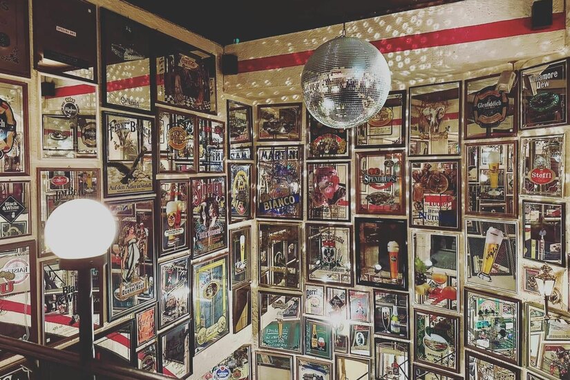 Innenansicht einer Bar mit vielen gerahmten Werbeplakaten an den Wänden und einer Discokugel an der Decke.