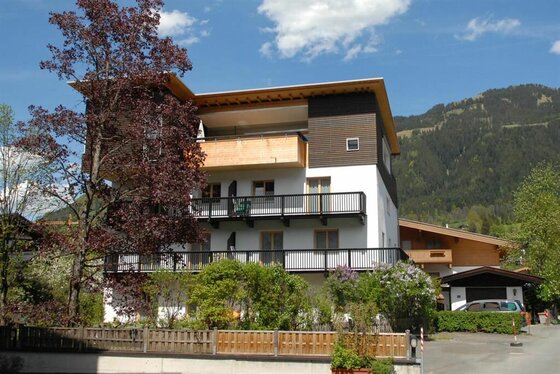 Gästehaus Maier im Sommer Mehrstöckiges Gästehaus mit Holzbalkonen vor bewaldetem Berghang unter blauem Himmel.