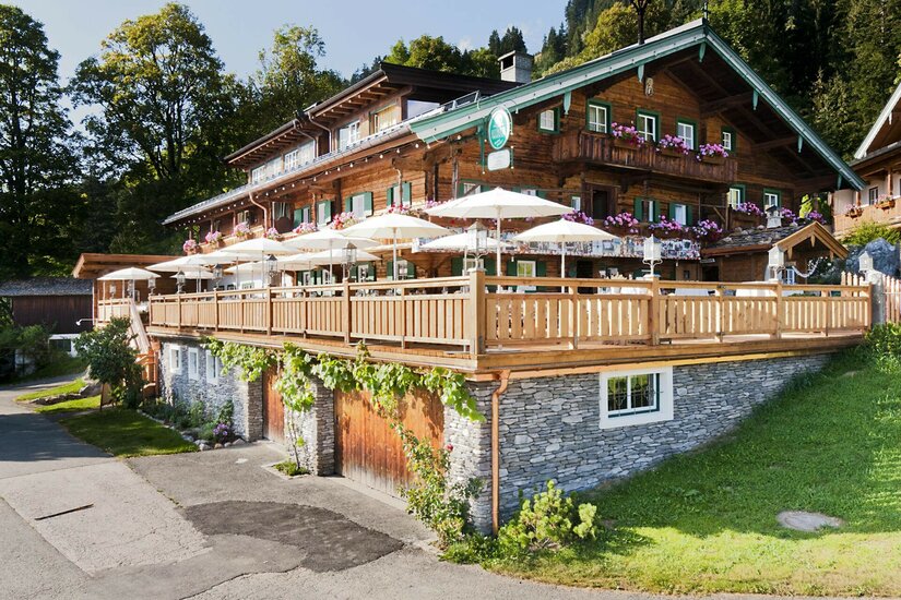 Gasthof Hagstein im Sommer Mehrstöckiger Gasthof aus dunklem Holz mit großer Sonnenterrasse und weißen Schirmen.