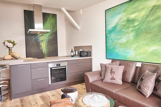 Moderne Küchenzeile mit Einbaubackofen neben einem braunen Ledersofa und großformatigen Wandbildern.