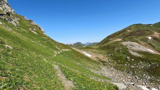 Wanderpfad am Berghang Schmaler Wanderpfad an einem grünen Berghang unter blauem Himmel.